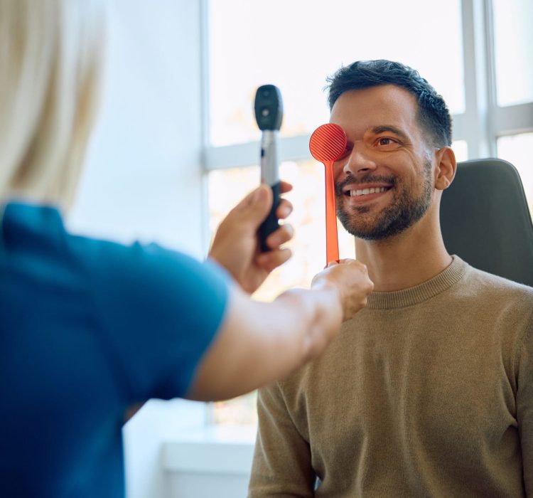 Young happy man getting his eyesight checked by female optometrist at eye clinic.